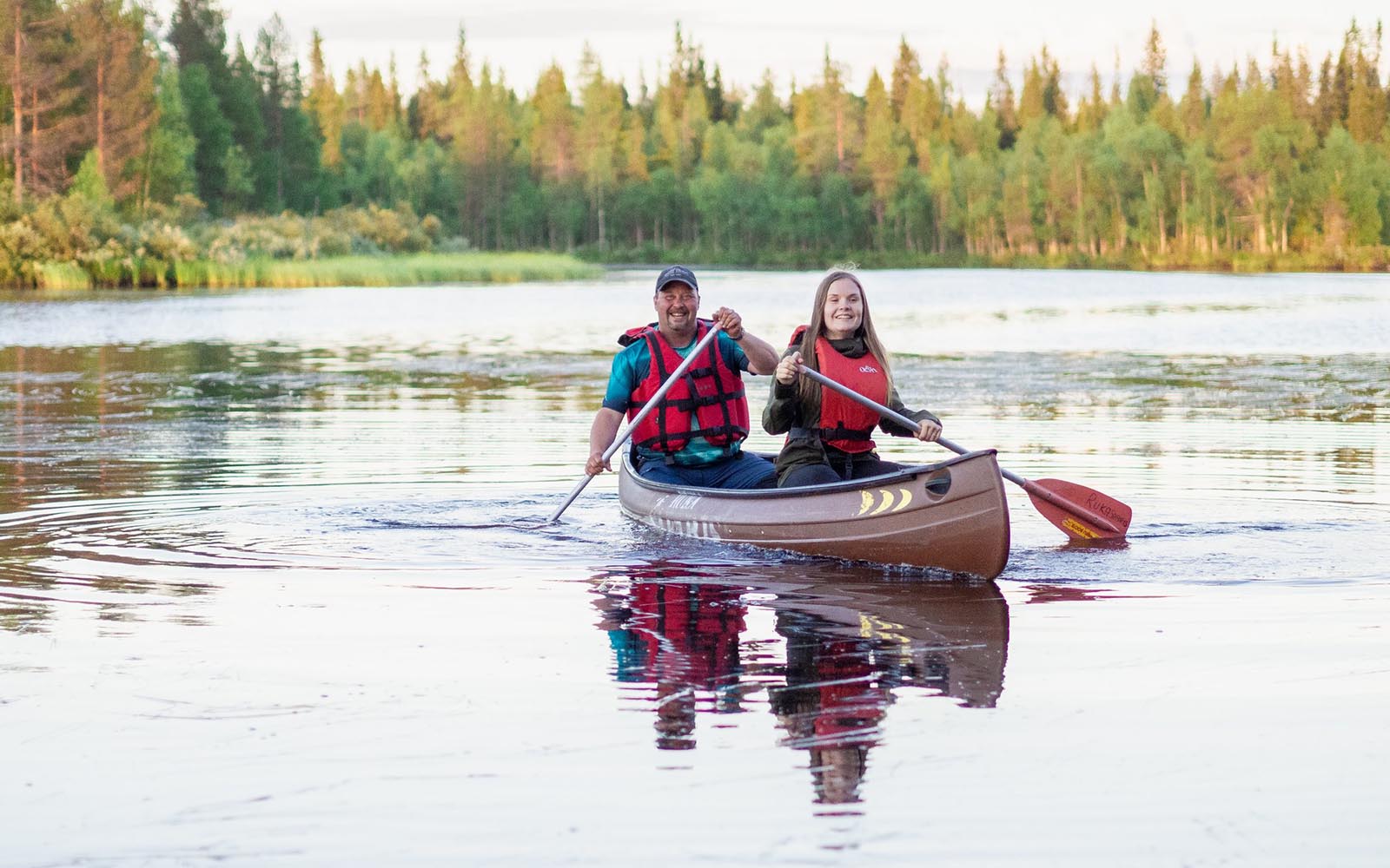 A man and women wearing red life jackets paddle a canoe on the lake at Iisakki Village in Finnish Lapland 