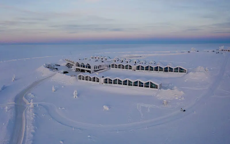 wide aerial view of the modern Star Arctic Resort nestled in a vast, snow-covered landscape. The buildings have a distinctive architectural style with zigzag rooflines and large glass windows facing outward for fabulous panoramic views