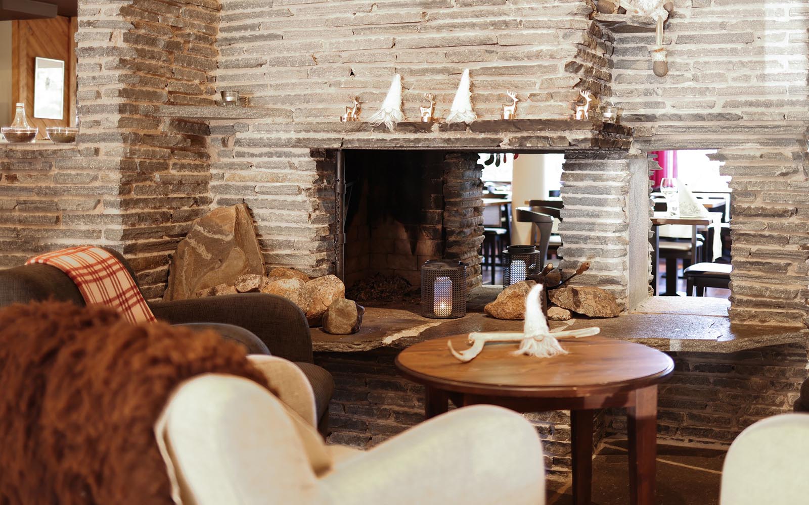 Cosy armchairs sit around a stone fireplace with gonks on the mantlepiece in the guest lounge at Santa's Hotel Aurora in Luosto, Finnish Lapland 