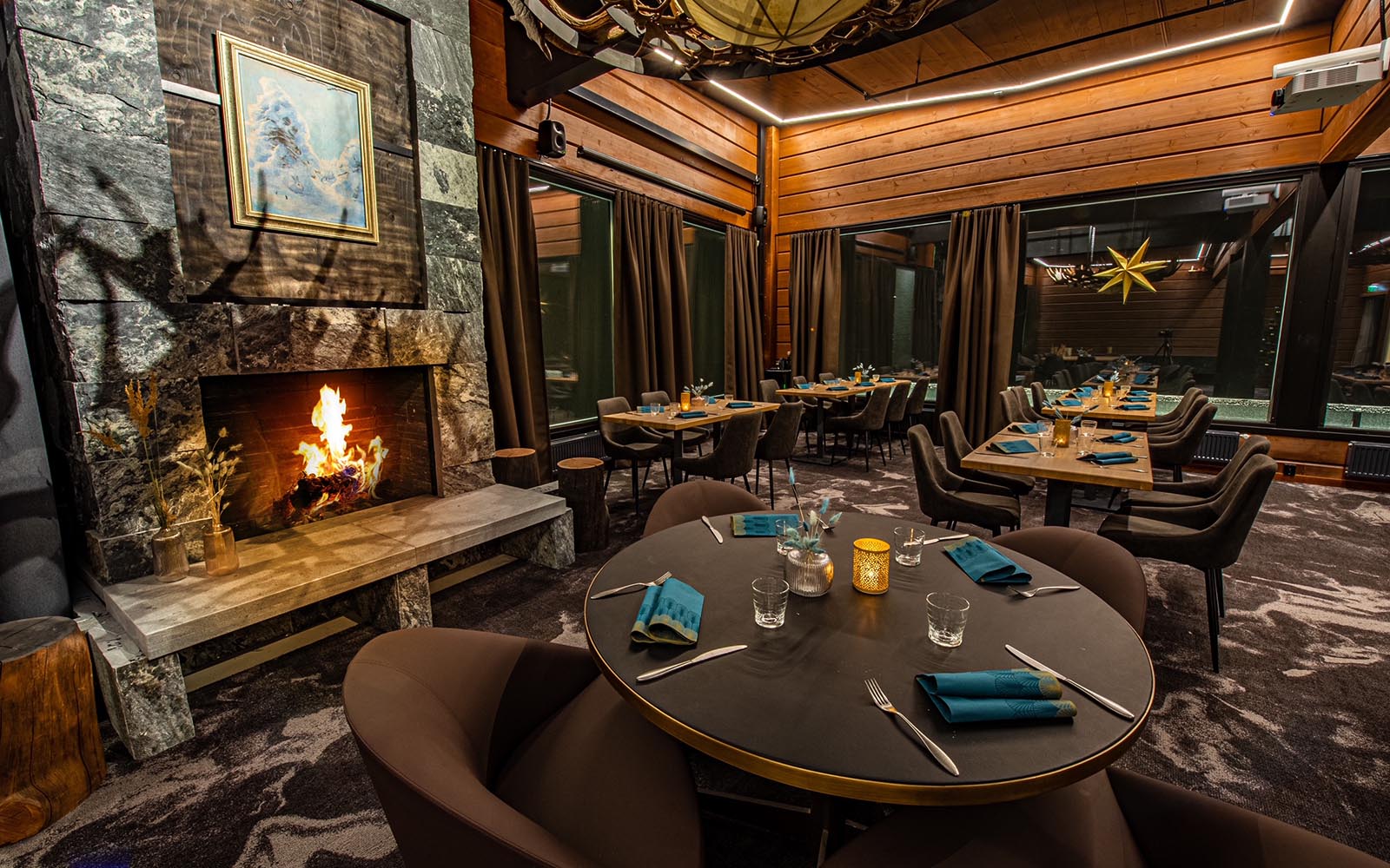 A cosy dinner table setting next to a roaring log fire at Hilltop Restaurant, Hotel Iso Syote in Finland
