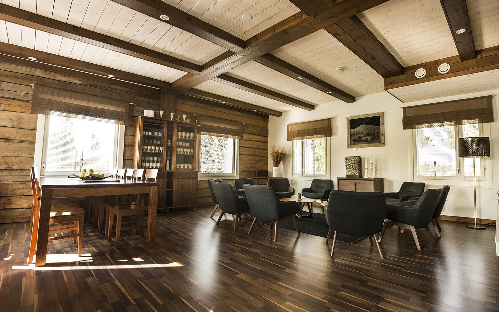 The welcoming communal lounge and dining area at Wilderness Hotel Papin Talo with polish dark wood floors and white wash ceiling framed by dark wood beams 
