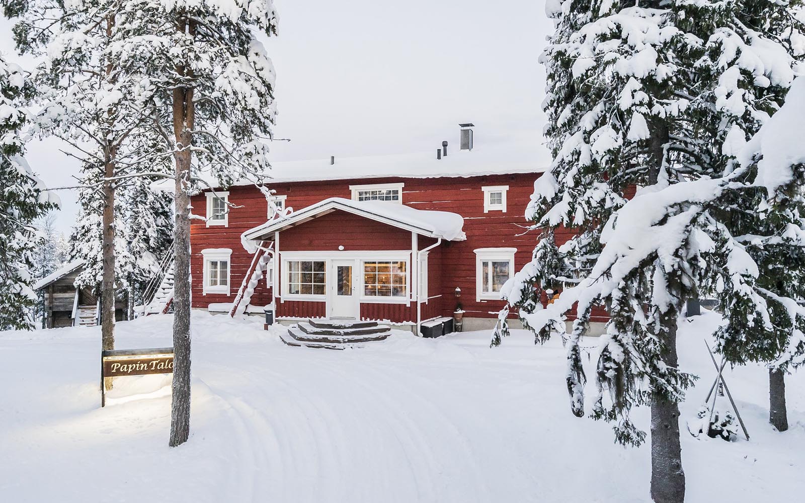 Framed by snow laden trees, Wilderness Hotel Papin Talo, with it's traditional Falun red painted exterior, sits in a winter wonderland setting at Iisakki Village in Finnish Lapland. 