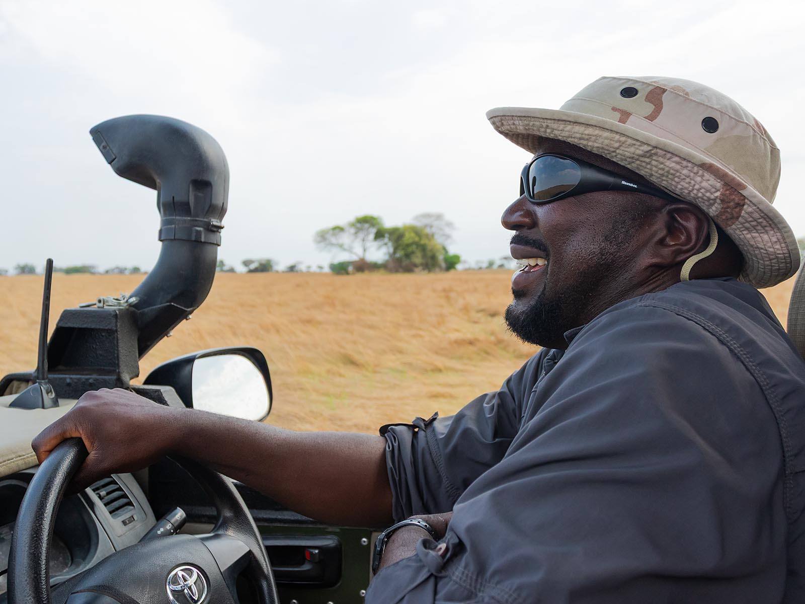 Guide Isaac smiling & driving on Busanga Plains, Kafue National Park; photograph taken on safari in Zambia by Wildlife & Wilderness