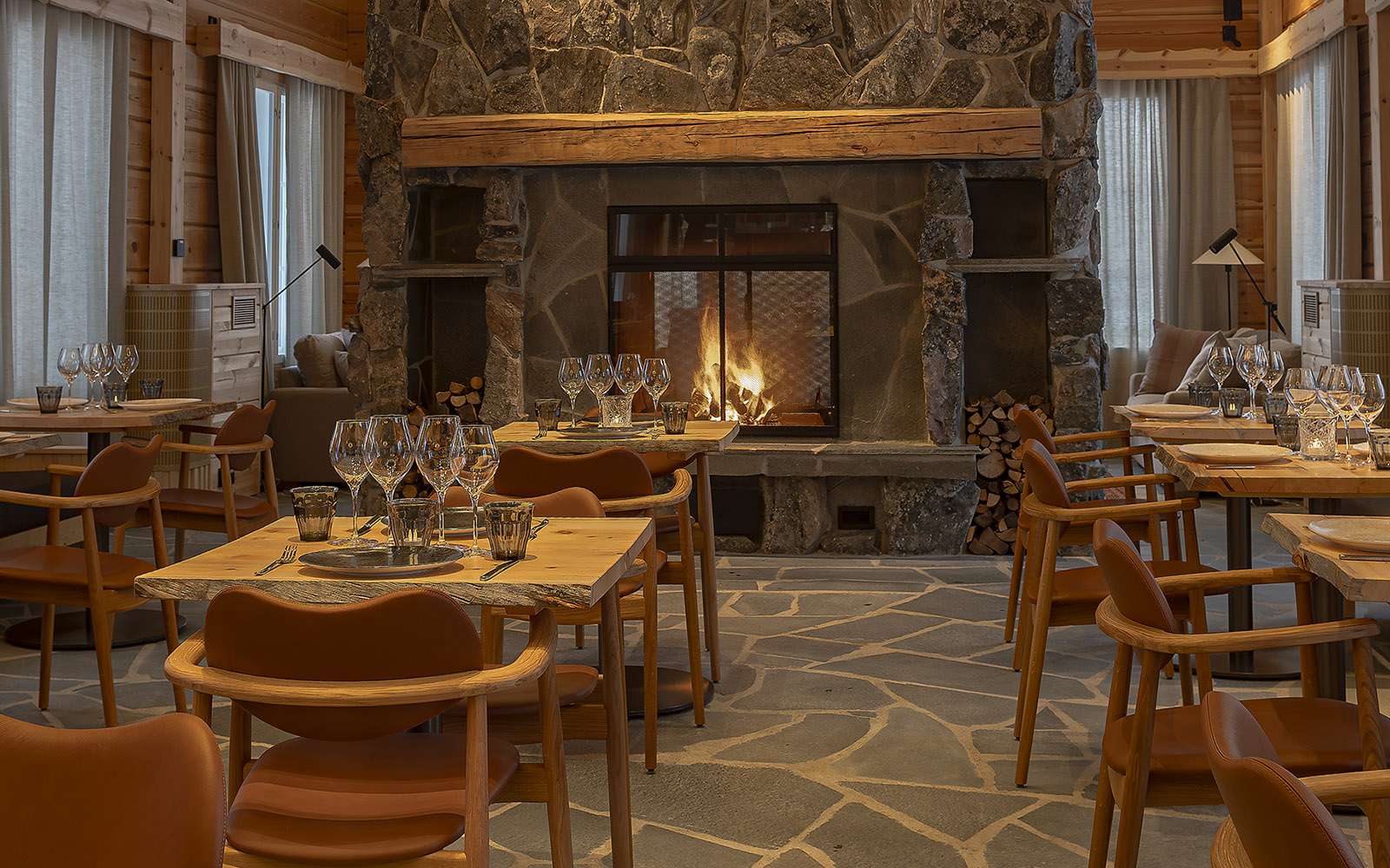 A contemporary pine clad restaurant with stone floor and a huge stone fireplace is dressed for dinner at Nivunki Village in Finnish Lapland