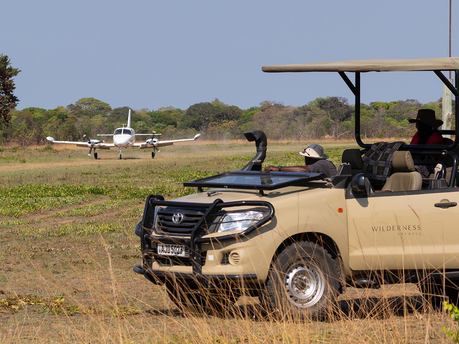Guests waiting in a safari vehicle as an aircraft lands in Busanga Plains, Kafue National Park; photograph taken on safari in Zambia - Wildlife & Wilderness