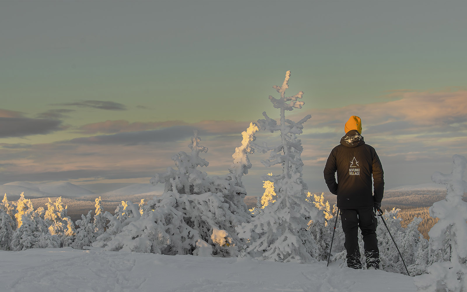 A person dressed in Arctic clothing stands in a snow covered landscape and soaks up the views from the top of a fell in Finnish Lapland during a snowshoe hike 