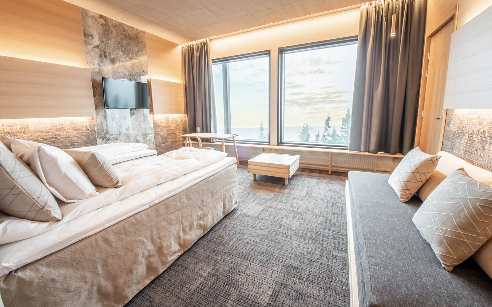Stunning views of the fell through the large picture windows in the Star Superior Room at Hotel Iso Syote, decorated in muted tones, there is a double bed and sofa bed 