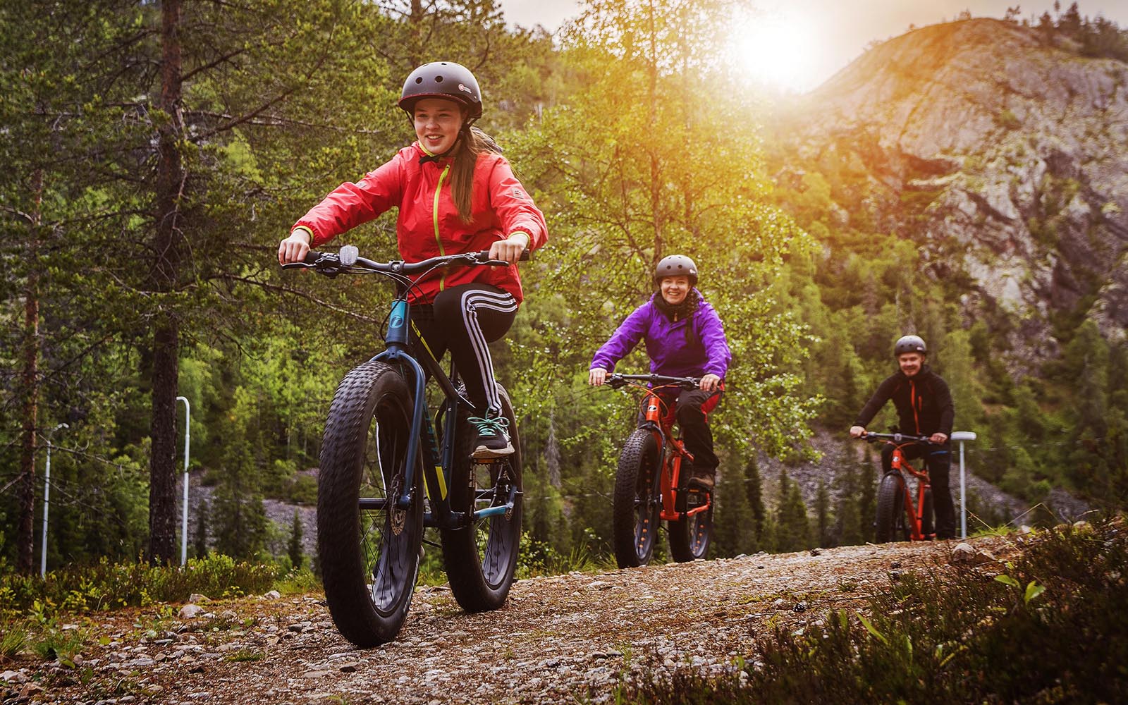 A family of 3 in casual clothes and bike helmets ride fat bikes though an autumnal Finnish forest in Ruka, Lapland