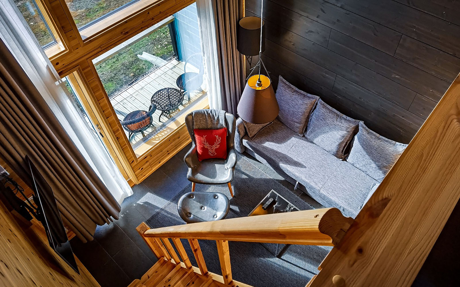 looking down on a cosy lounge area from the top of the wooden stairs of the mezzanine bedroom in the Aurora Glass Cabin at Star Arctic Resort in Saariselka, Finnish Lapland 