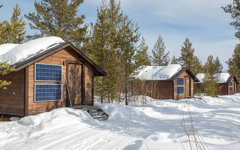 Image of the exterior of the sleeping cabins among the trees at Polar Lights Tours in snowy winter and sunshine, photograph by Wildlife & Wilderness