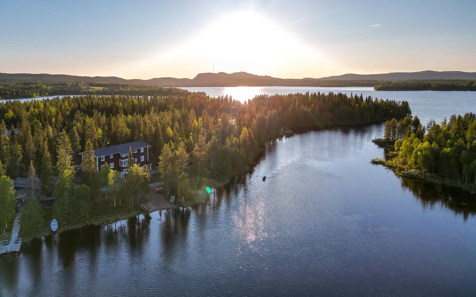 an aerial drone image shows Wilderness Hotel Papin Talo nestled amongst the trees and surrounded by the lakes at Iisakki Village in Finnish Lapland 
