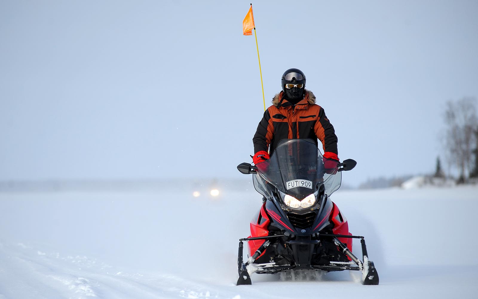 A solo rider on a red and black snowmobile with an orange flag sticking up on the back rides along the frozen Bothnian Bay from Brandon Lodge