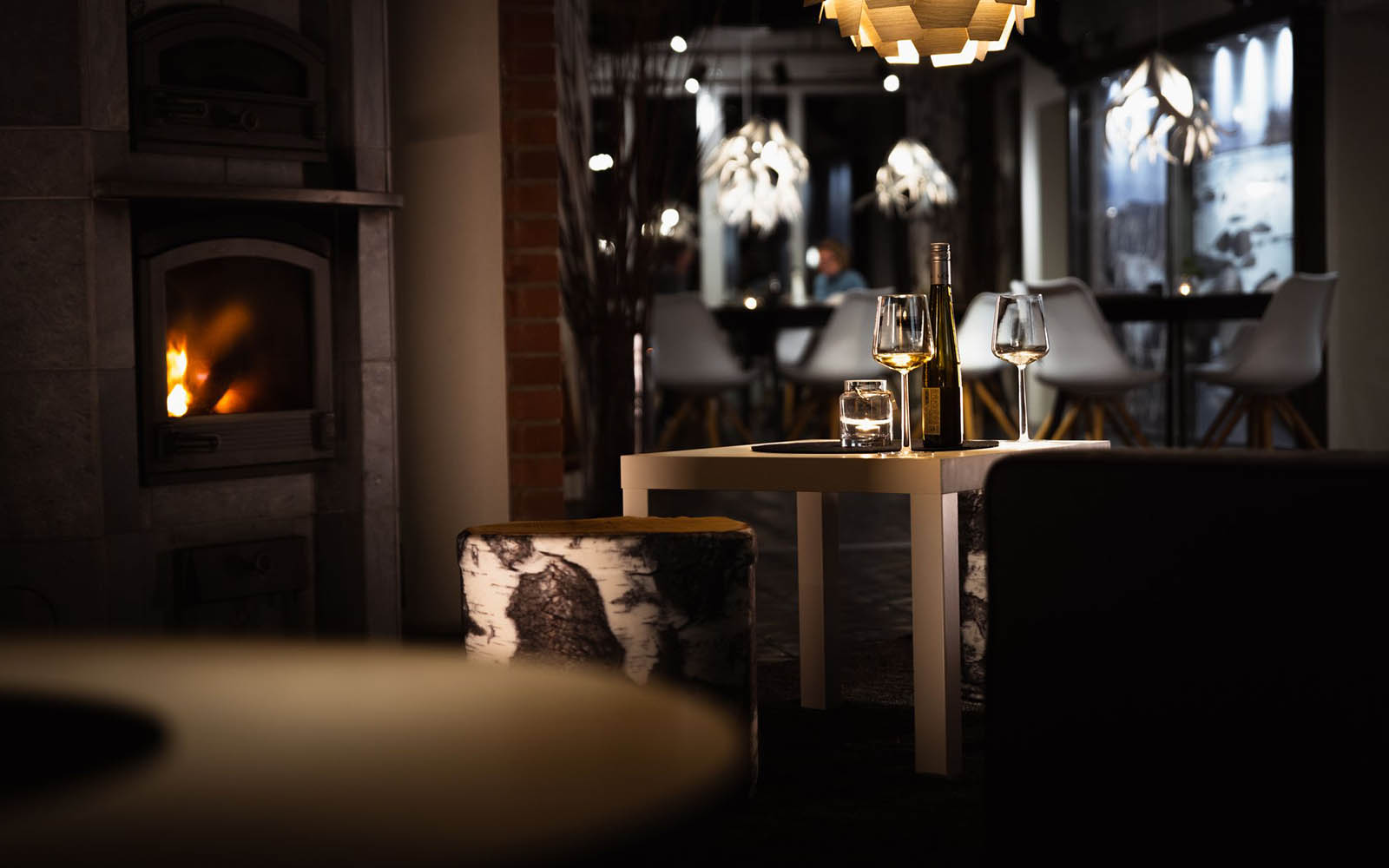 Wine sits on the table in the cosy and dimly lit guest lounge at Mattarahkka Northern Lights Lodge.  The log burner is lit and you can see beyond to the restaurant.