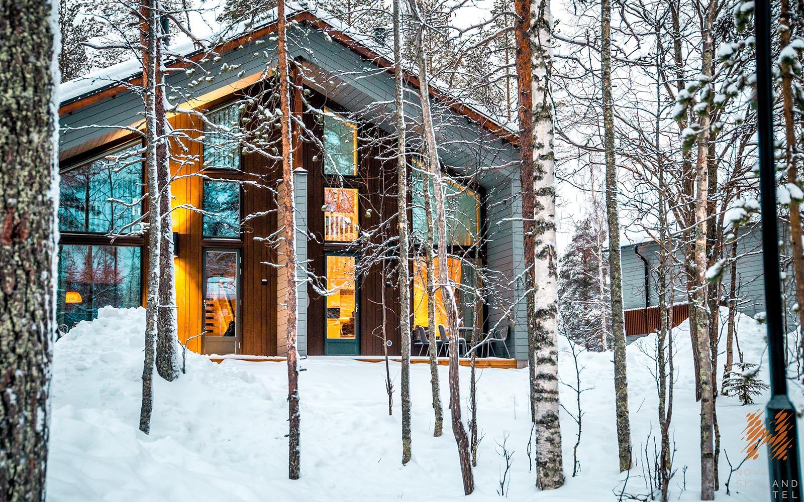 Looking through the trees across the snow towards the Nordic Cottage, family accommodation at Nova Skyland, near Santa Claus Village in Finnish Lapland 