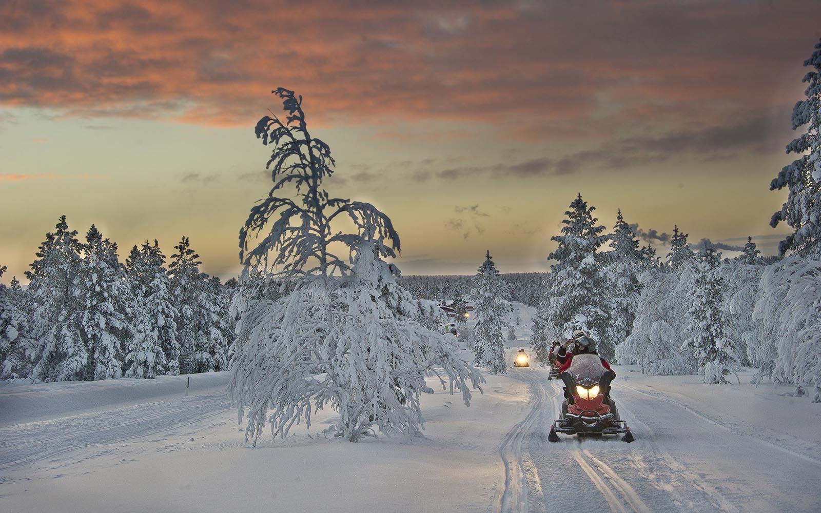 a snowmobile travels along a snowy frozen trail in Finnish Lapland, the clouds in the sky glow orange in the polar night