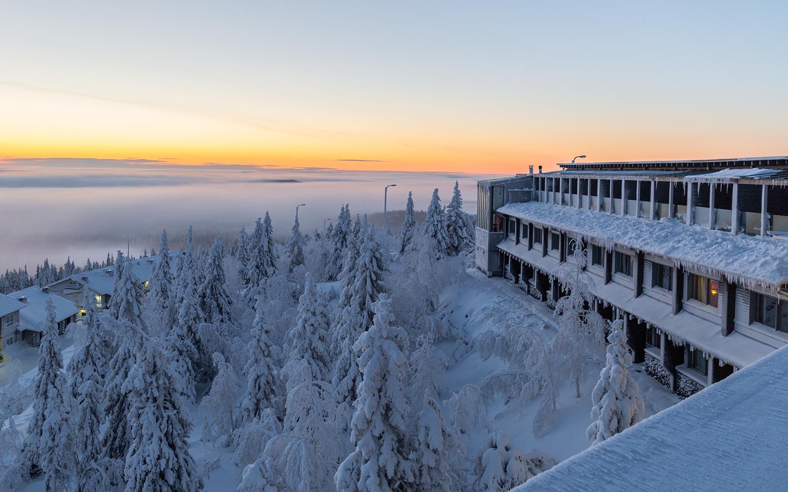 a winter view from an outdoor balcony at Hotel Iso Syote, Finland showing the side elevation of the main hotel building, the surrounding landscape is covered in snow and clouds sit in the valley below 