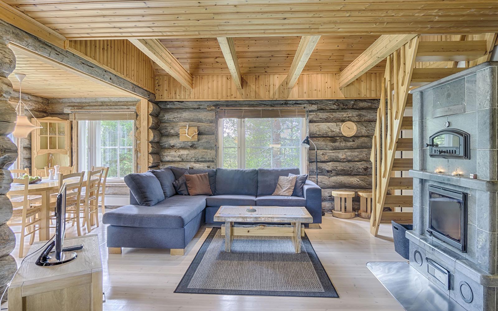 The open plan lounge area of Villa Rukan Huurre at Iisakki Village in Finnish Lapland, boasts a huge fireplace, exposed log walls and pine clad ceiling. 
