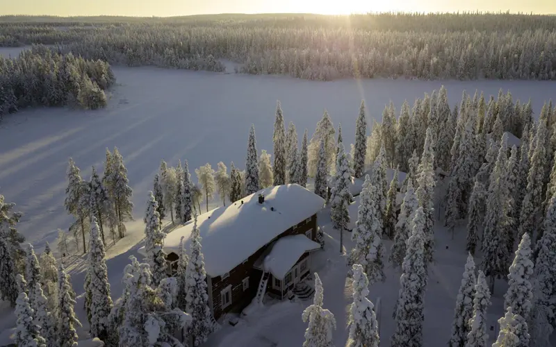 An aerial view of Wilderness Hotel Papin Talo surrounded by snow laden trees and the frozen lake at Iisakki Village near Ruka in Finnish Lapland