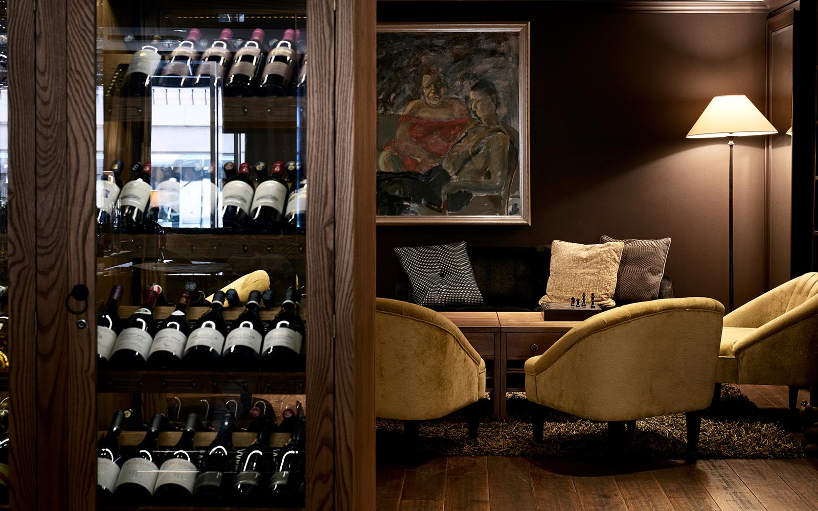 The cost guest lounge and bar at Hotel Haven in Helsinki with luxurious yellow bucket chairs and a wood and glass wine cabinet stocked with bottle of wine
