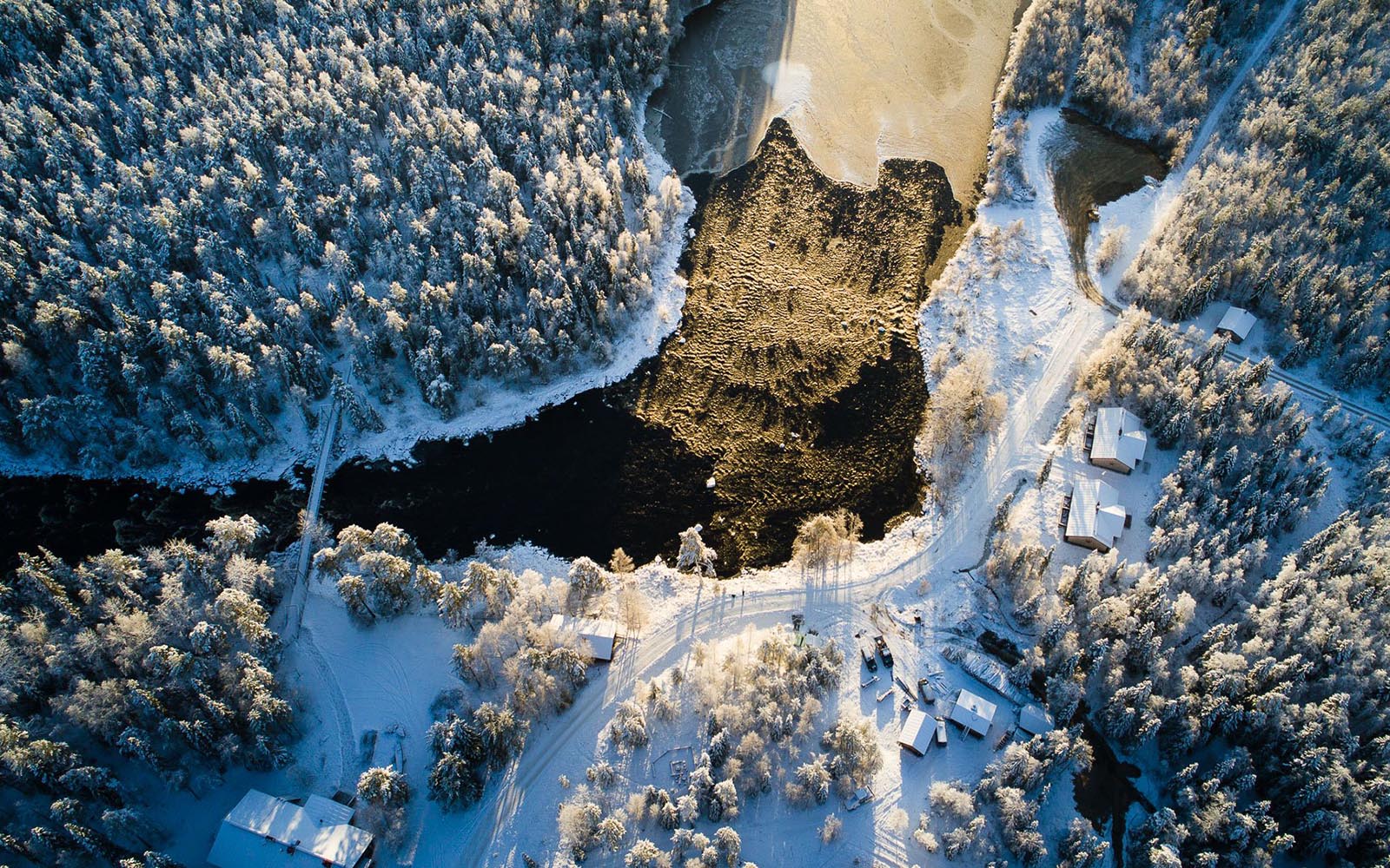 an aerial image taken by drone of the river rapids and log buildings in winter in a snowy setting at Vaattunki Wilderness Resort near Rovaniemi in Lapland, Finland