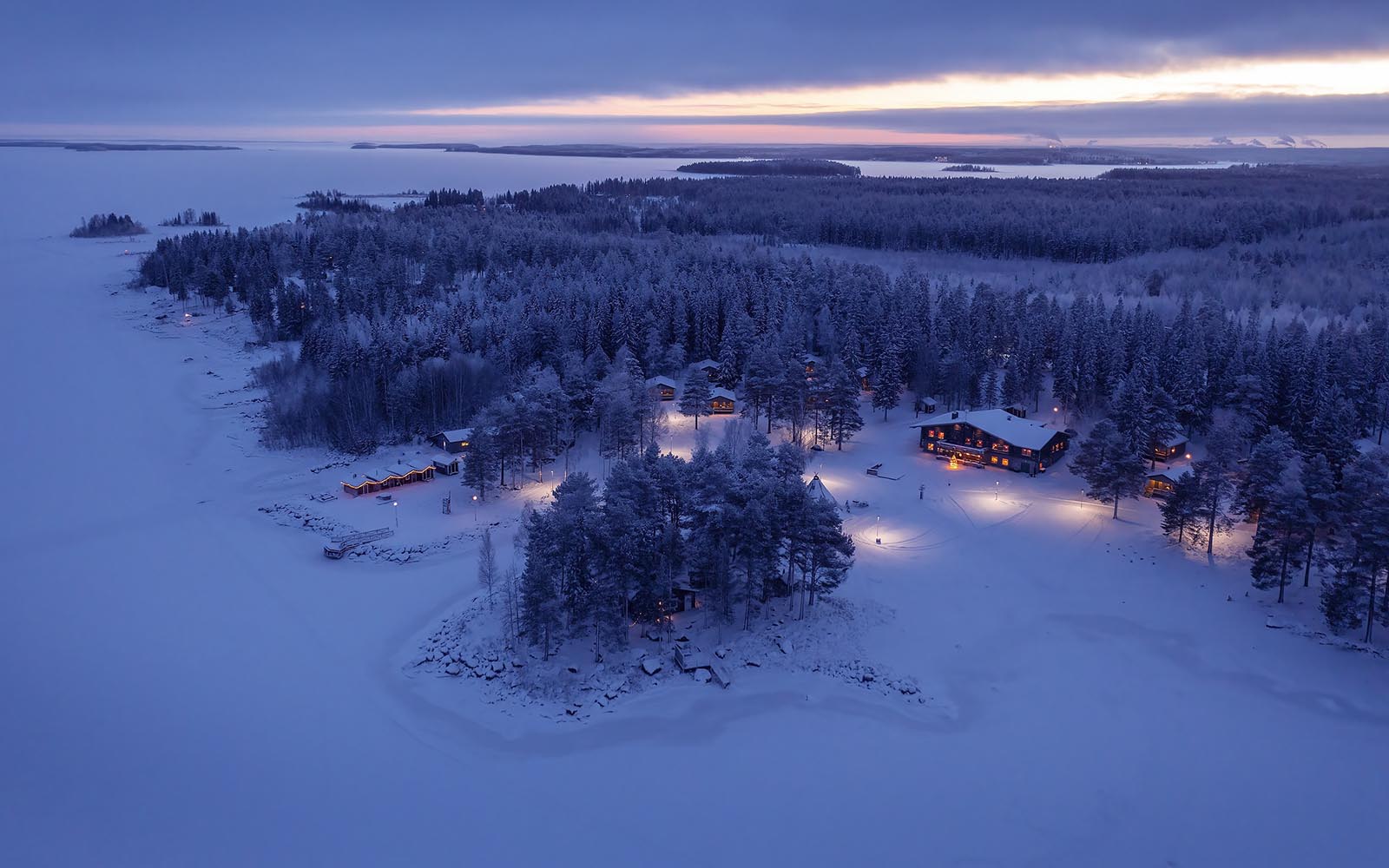 A aerial shot at dusk of Brandon Lodge on the Luleå archipelago shows the vast expanse of the frozen Bothnian Sea with the Lodge building set amongst the trees 