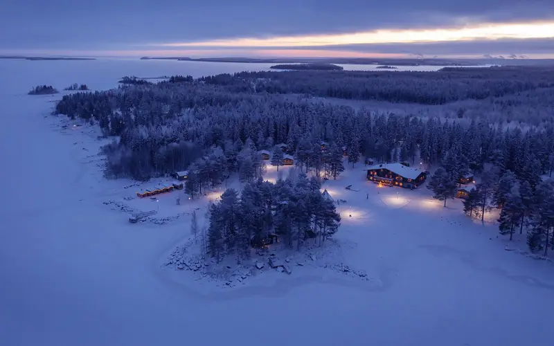 A aerial shot at dusk of Brandon Lodge on the Luleå archipelago shows the vast expanse of the frozen Bothnian Sea with the Lodge building set amongst the trees