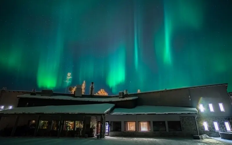 Santa's Hotel Aurora in Luosto, Finnish Lapland sits under a night skies streaked with turquoise and green northern lights (aurora borealis)