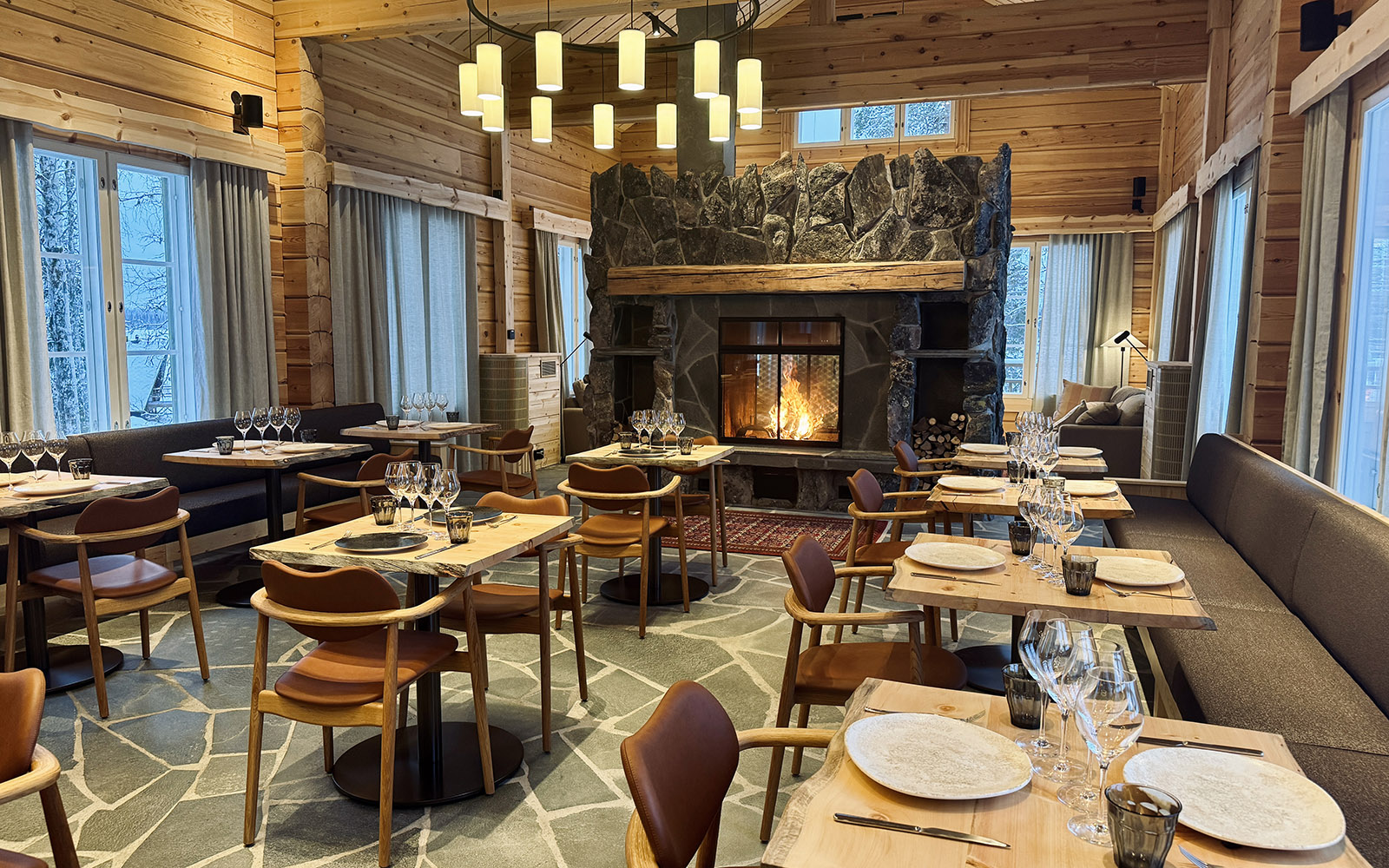 A contemporary pine clad restaurant with stone floor and a huge stone fireplace is dressed for dinner at Nivunki Village in Finnish Lapland