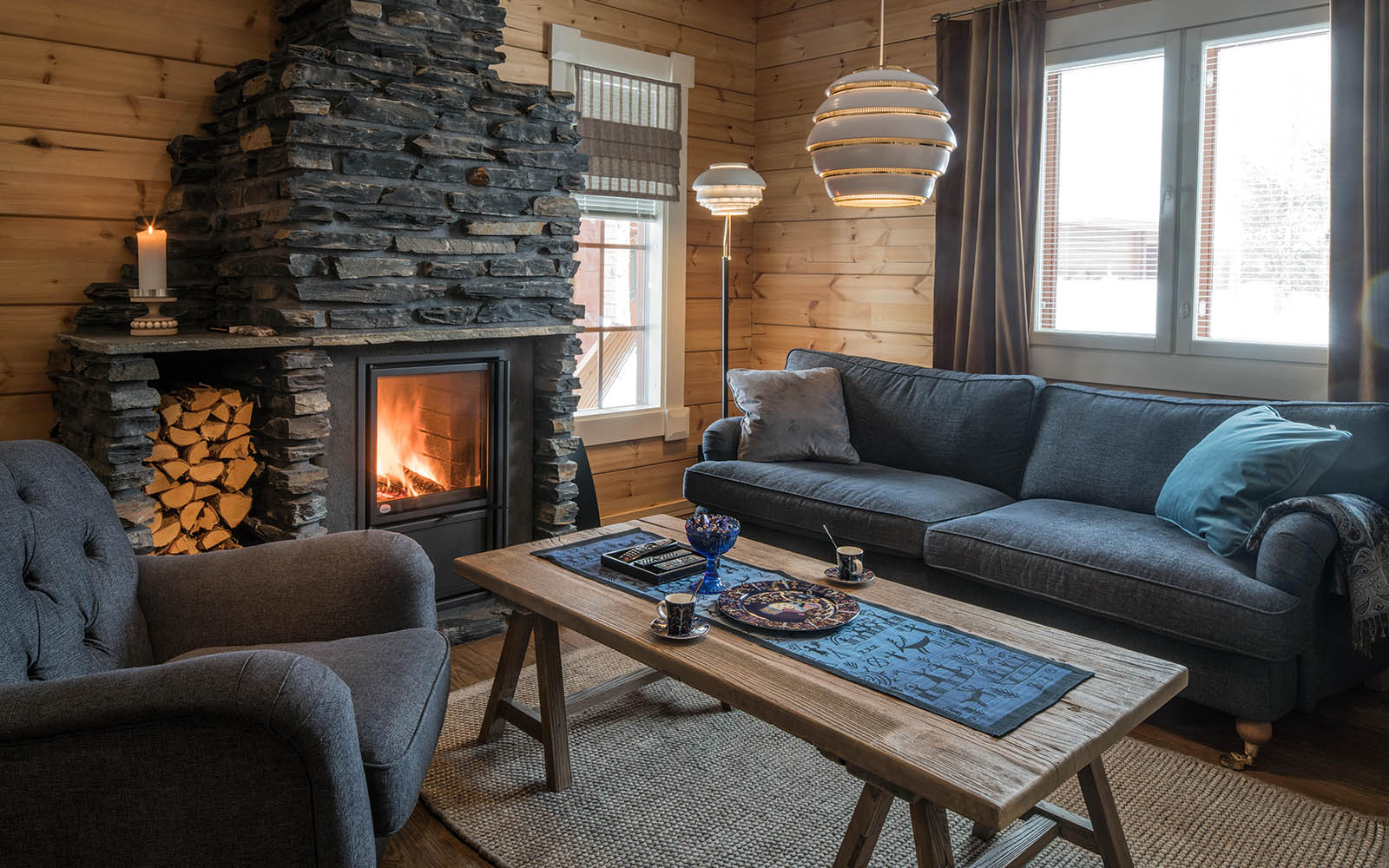 The comfortable lounge in the Suite at Hotel Yllas Humina in Finland offers a sofa, armchair and a roaring log fireplace stacked with plenty of firewood.