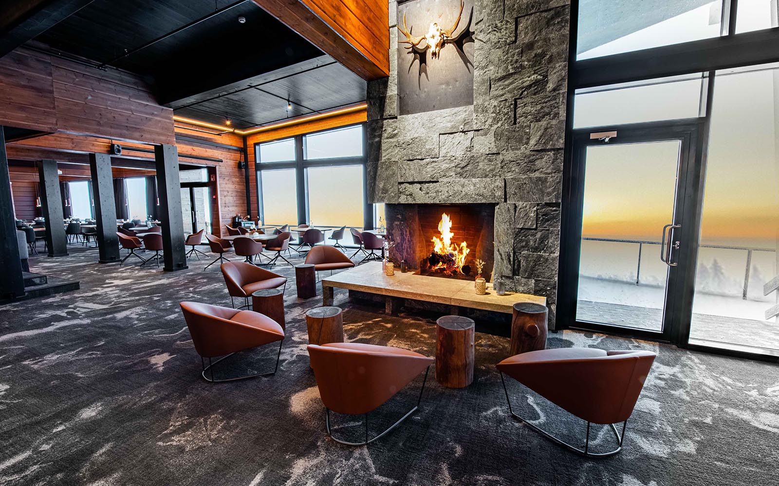 5 tan leather bucket chairs are arranged next to log tables and a roaring log fire in the guest lounge at Hotel Iso Syote in Lapland, Finland. 