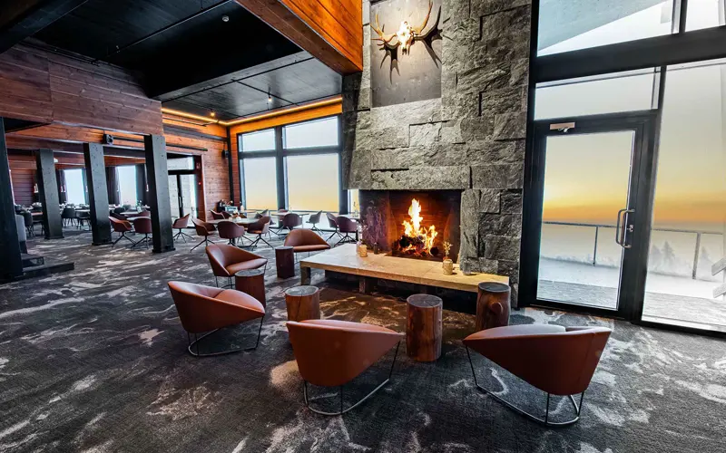 5 tan leather bucket chairs are arranged next to log tables and a roaring log fire in the guest lounge at Hotel Iso Syote in Lapland, Finland.