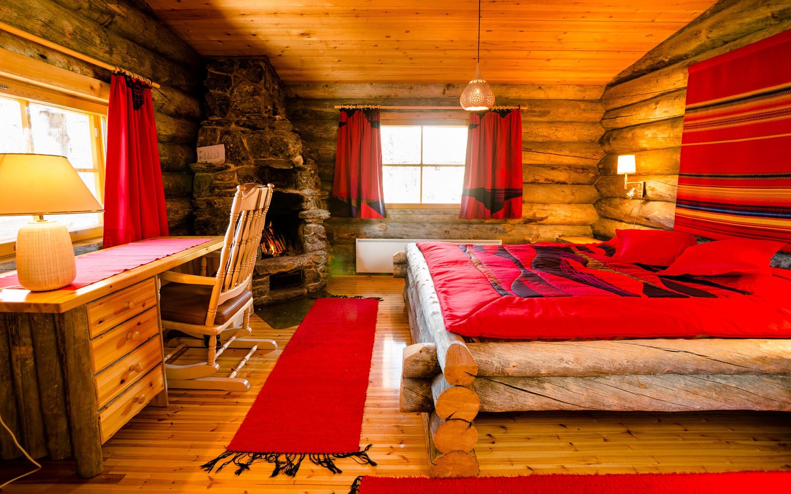 The interior of a small kelo log cabin in East Village at Kakslauttanen Resort in Finnish Lapland with a huge log built bed and red soft furnishings 