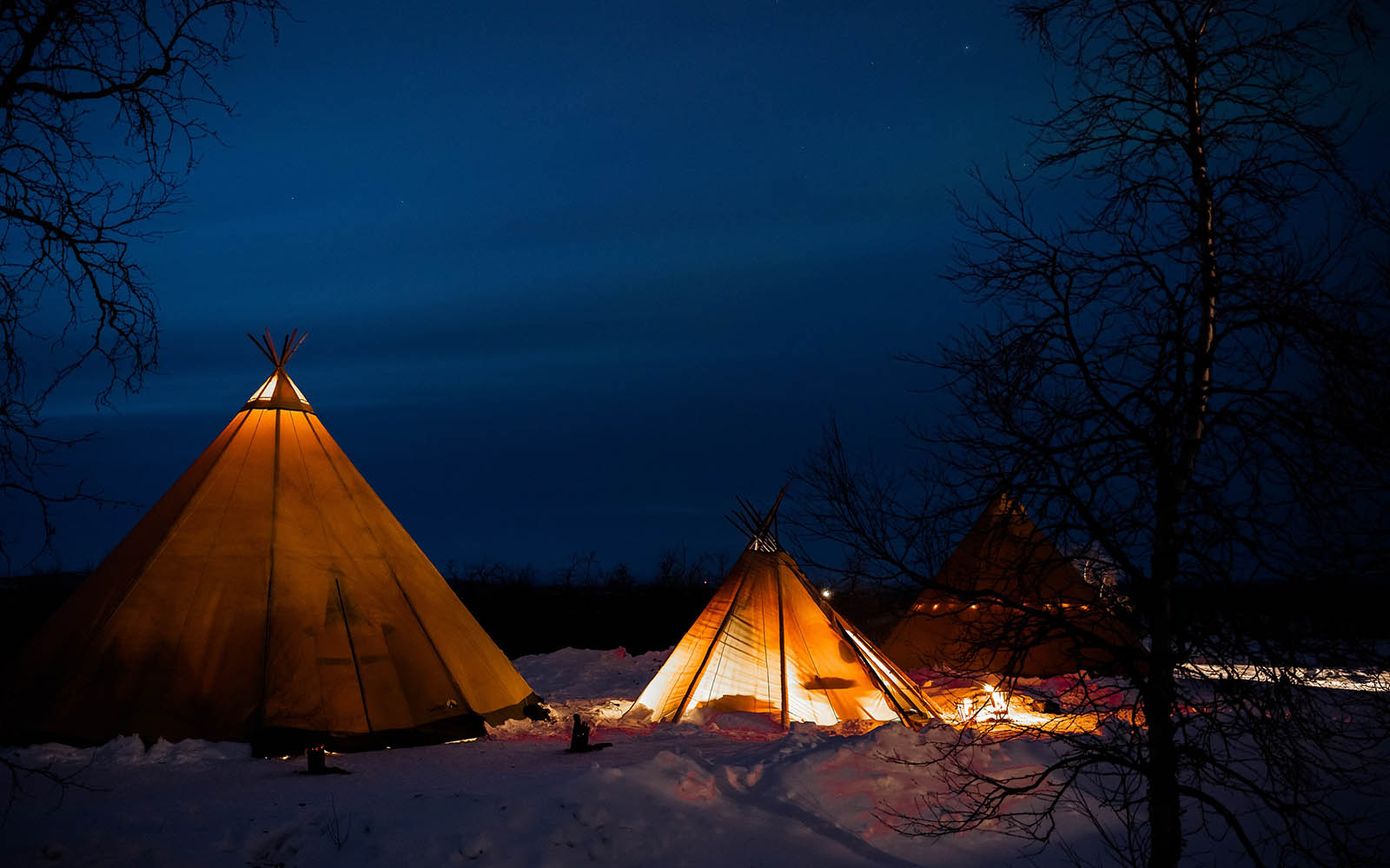 Three tipis (laavu) outside Mattarahkka Northern Lights Lodge in Swedish Lapland where wilderness BBQ dinner are served.