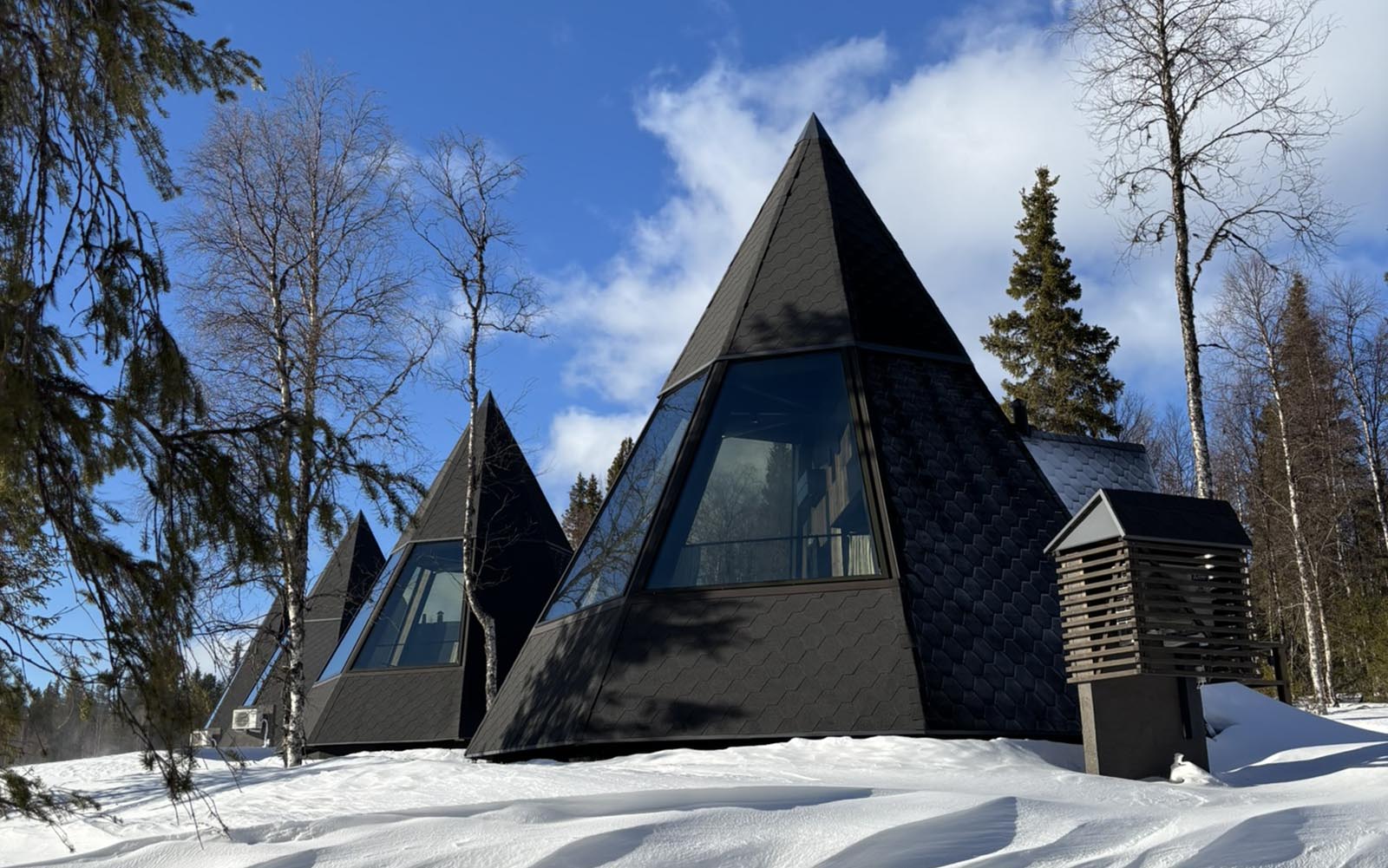 Modern architecturally designed cone shaped Kota Aurora Huts are nestled in the snow with a bright blue sky in the background at Nivunki Village in Finnish Lapland