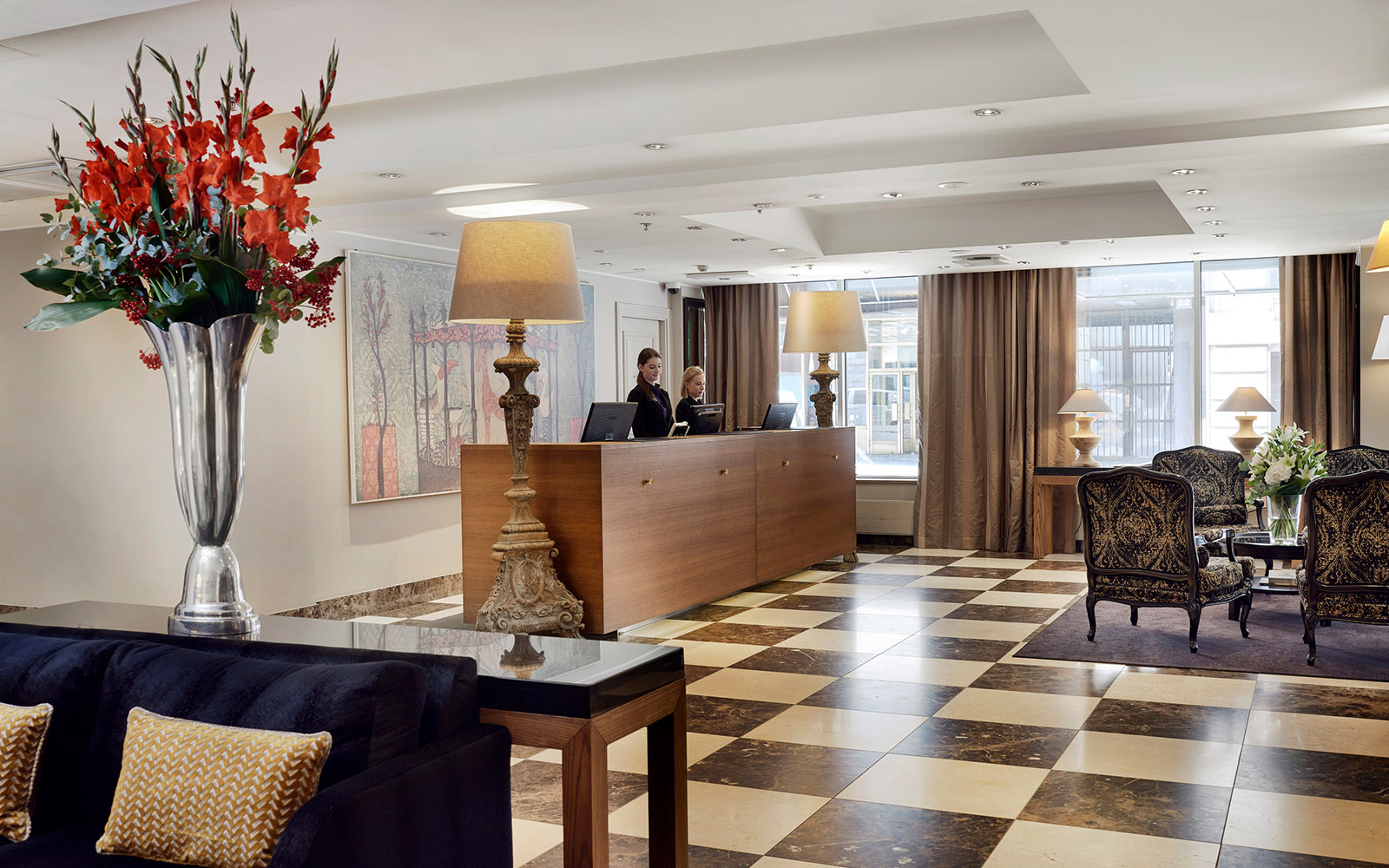 The reception area at Haven Hotel Helsinki with a checkered floor, comfortable seating area and a beautiful vase of flowers on a console table